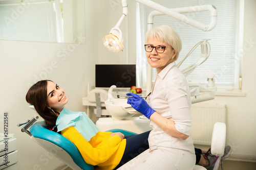Portrait of a smiling woman, sitting at the dental chair with doctor at the dental office