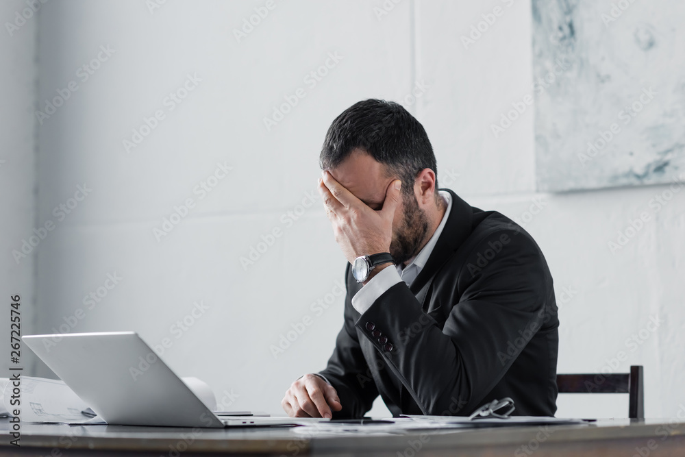 upset businessman holding hand on face while sitting at workplace upset businessman holding hand on face while sitting at workplace