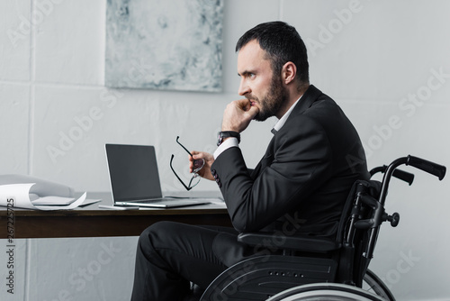 disappointed disabled businessman sitting in wheelchair at workplace photo