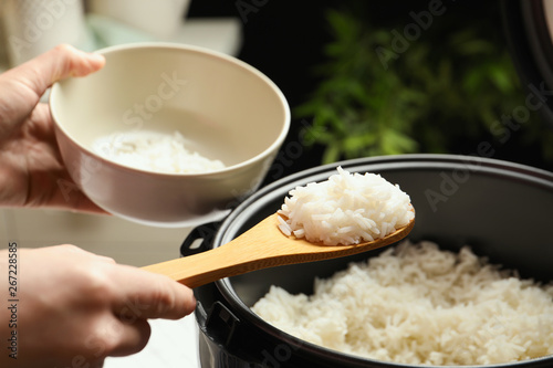 Photos Woman putting tasty rice into bowl from cooker in kitchen, closeup