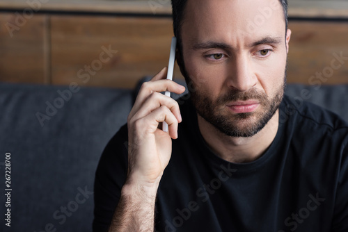 upset bearded man in black t-shirt using smartphone while sitting at home
