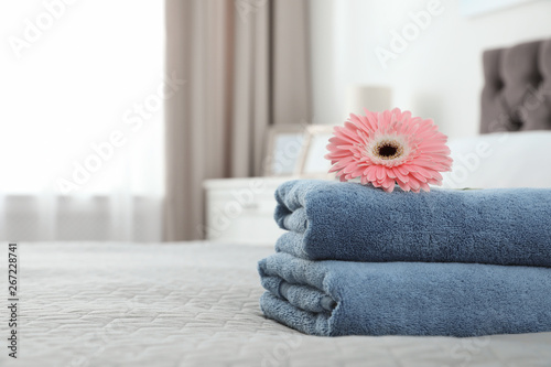 Stack of clean towels with flower on bed indoors. Space for text