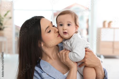 Happy young mother kissing her adorable baby in living room