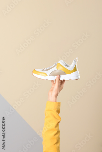 Woman holding sportive shoe on color background, closeup. Space for text