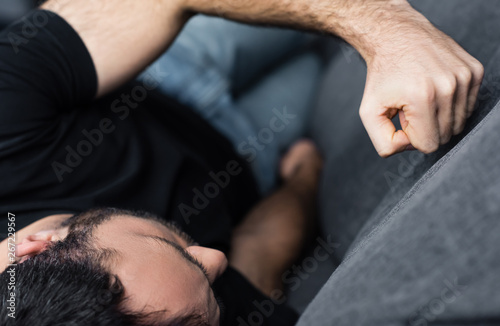 selective focus of depressed man lying and kicking sofa with fist