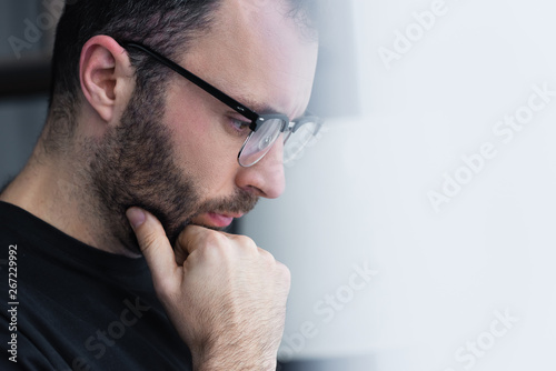 selective focus of thoughtful man in glasses holding hand near face and looking down