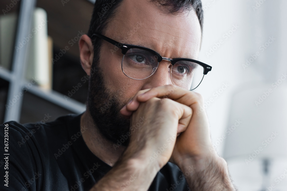 handsome depressed man in glasses holding folded hands near face