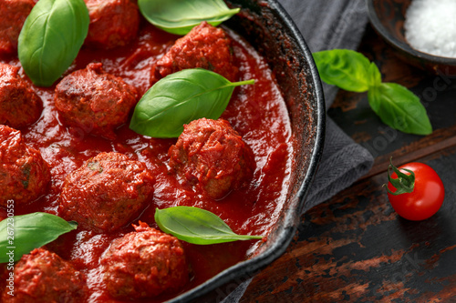 Homemade Meatballs in iron cast with sweet and hot tomato sauce, basil. On wooden table