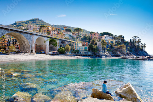 Fototapeta Little kid boy climbing on stones on beach of Mediterranean sea in Liguria region, Italy