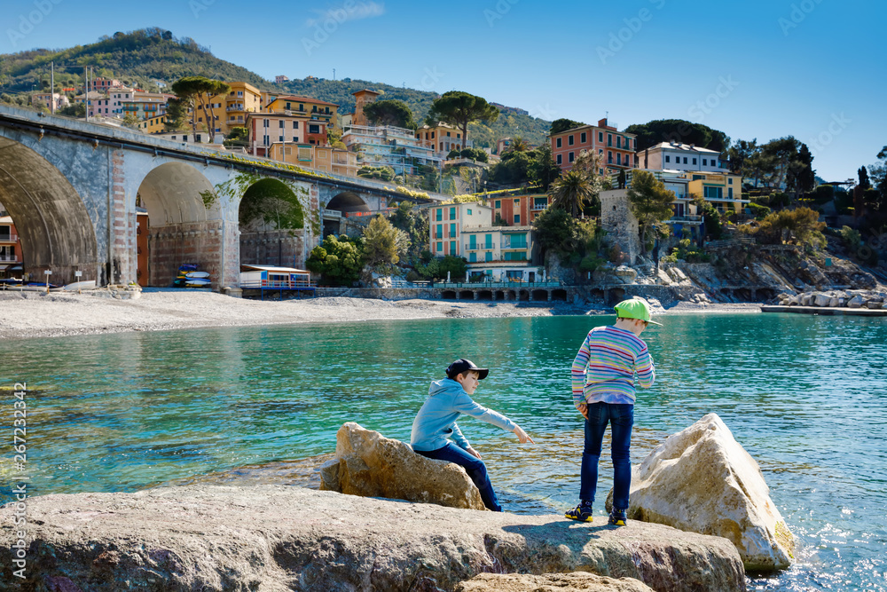 Φωτογραφία Two little kids boys climbing on stones on beach of Mediterranean sea in Liguria region, Italy