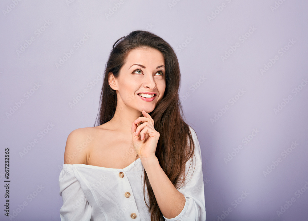 Beautiful positive young casual woman with hand under the face thinking and looking up in white shirt on purple background Beautiful positive young casual woman with hand under the face thinking and looking up in white shirt on purple background