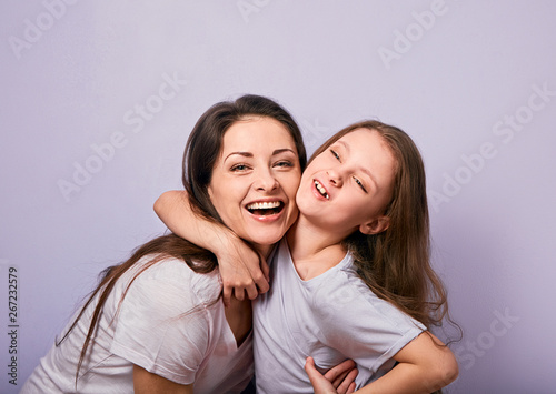 Happy mother and excited joying kid girl hugging with emotional smiling faces on purple background with empty copy space.