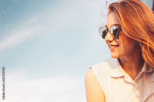 Positive beautiful happy red haired girl in the mirror sunglasses on blue sky background, summer sunset time © Galina Zhigalova