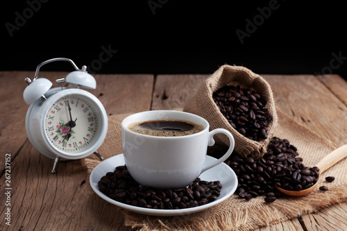 White Coffee cup with white alarm clock and coffee beans on old wood plank background
