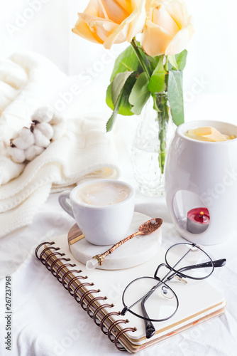 Morning coffee mug with glasses on a notebook, candle and rose on a white bed top view . Woman cozy morning