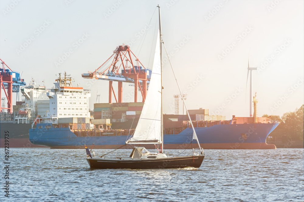 Segelschiff auf der Hamburger Elbe vor Containerschiff und Hafen in der Abendsonne