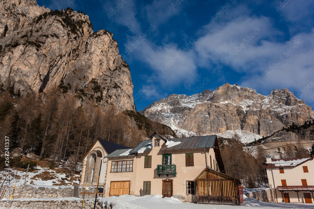 Pian Falzarego, Italy - 2019 January 21: Beautiful tiny Village in the Dolomite Mountains with massive rocky Mountains in the Background on a perfect sunny Winter Day