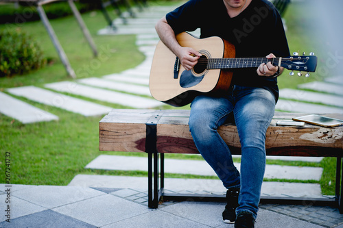 Picture of a guitarist, a young man playing a guitar while sitting in a natural garden,music concept