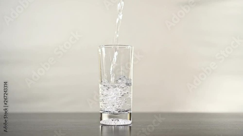 Pouring water into a glass until it overflowsPouring glass of water in slow motion until it overflows. Overfilling the liquid until the water flows onto the table.