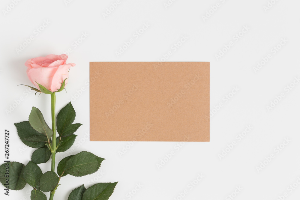 Fototapeta premium Top view of a kraft card mockup with a pink rose on a white table.