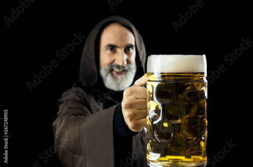 An old friendly friar (Franciscan religious man), offering a giant mug full of fresh beer to the viewer. photo