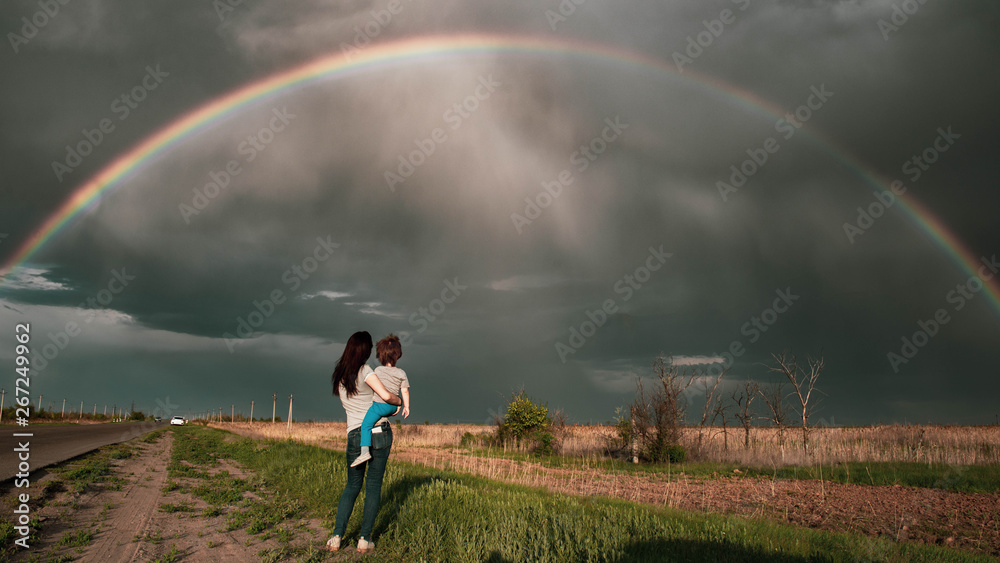 Rainbow over field with people. Mom and son look at the rainbow Rainbow over field with people. Mom and son look at the rainbow