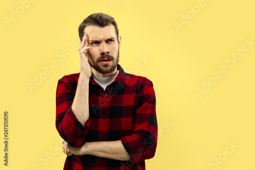 Half-length close up portrait of young man in shirt on yellow background. The human emotions, facial expression concept. Front view. Trendy colors. Negative space. Seriously thinking . © master1305