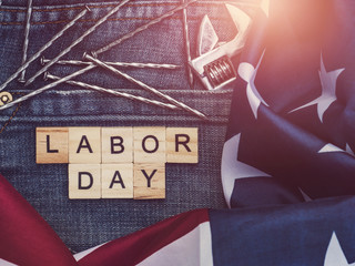 LABOR DAY. American Flag, wrench, nails, stylish jeans and wooden letters of the alphabet. Top view, close-up. Preparations for celebration. Congratulations for relatives, friends and colleagues