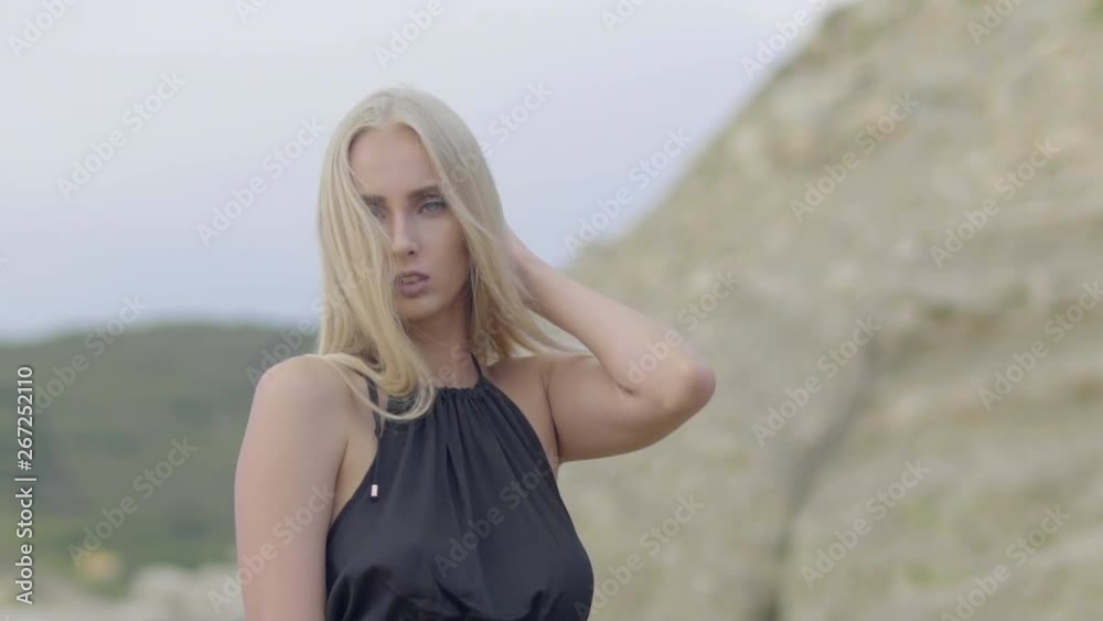 Attractive blonde woman posing at the beach,with blurred mountains in foreground, in the afternoon in 4K slow motion. Attractive blonde woman posing at the beach,with blurred mountains in foreground, in the afternoon in 4K slow motion.