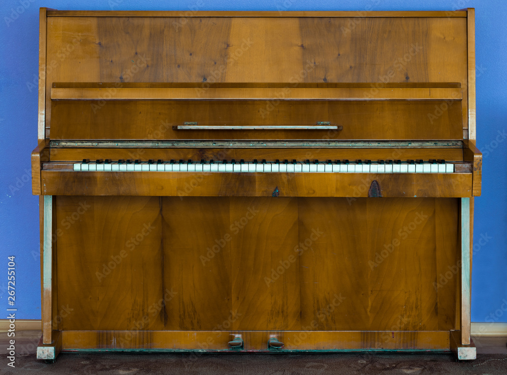 Old wooden piano. Brown piano stands against the wall Old wooden piano. Brown piano stands against the wall