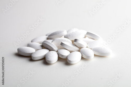 Pile of white drug pills laying on white background. Medical concept.