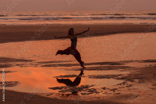 A cheerful girl runs at sunset along a sandy beach. Goa, rest. Indian Ocean. Freedom. Adventure. Excitement. Games. Reflection in water.