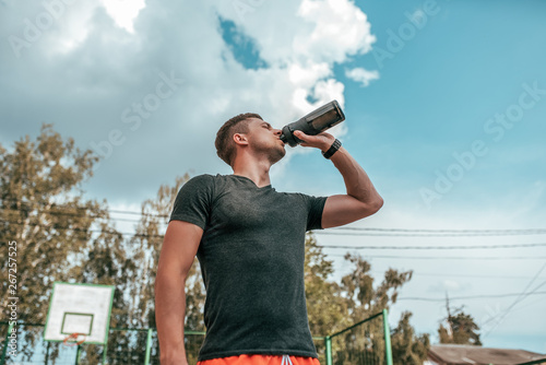 Male athlete, drinking water and protein from shaker, fitness watch, training in the city in the fresh air. Concept morning run in the city, fitness and workout, smart watch bracelet. Sportswear T
