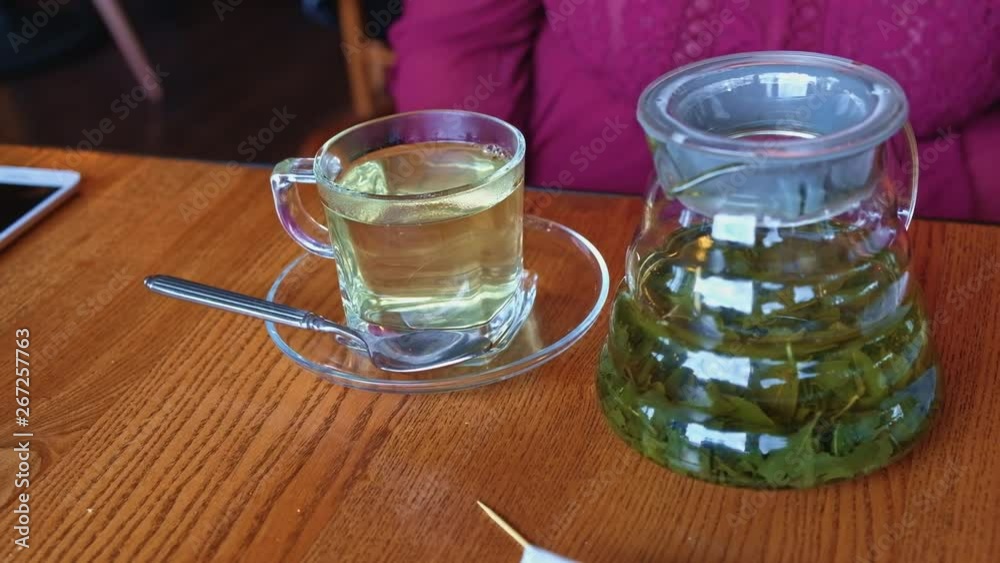 Glass tea cup with green tea and transparent tea infuser on the table in canteen Glass tea cup with green tea and transparent tea infuser on the table in canteen