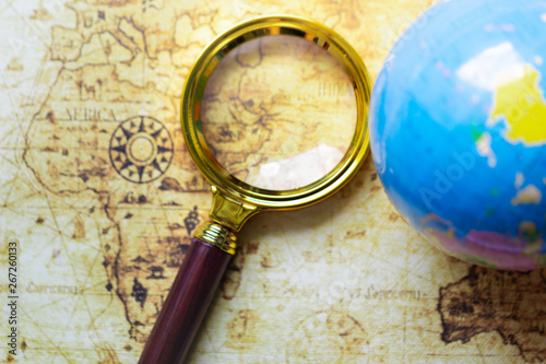 Magnifier and globe on old map background. Travelling concepts. Travel the world monument concept.