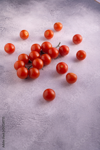 Bunch of cherry tomatoes on white textured stone concrete table, side view with copy space. Ingredients for cooking.