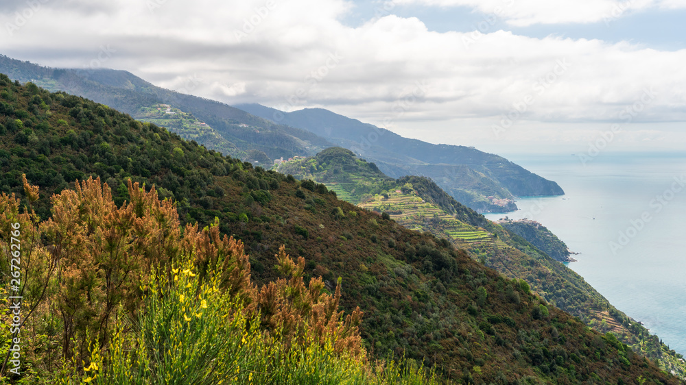 Coastline landscape with rolling hills and mountains on a spring day. View from the red hiking path between Monterosso and Vernazza in Cinque Terre, Italy, over the Ligurian Sea.