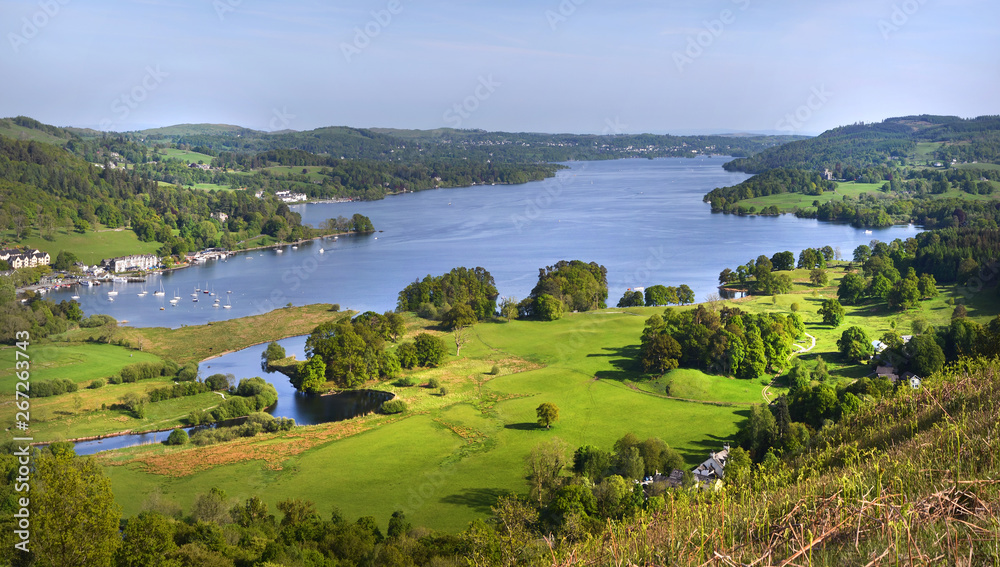 A panoramic view of a calm Lake Windermere taken from above Ambleside showing the land and yachting marina in the distance