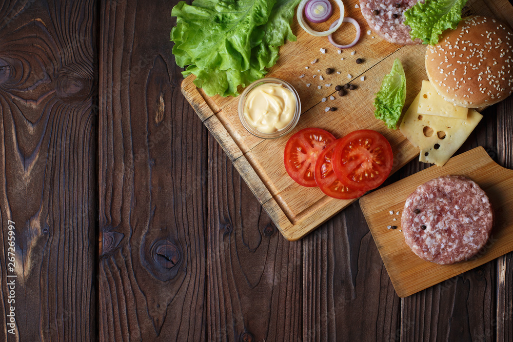 Raw ingredients for delicious home-made burger with copy space on dark wooden table Raw ingredients for delicious home-made burger with copy space on dark wooden table