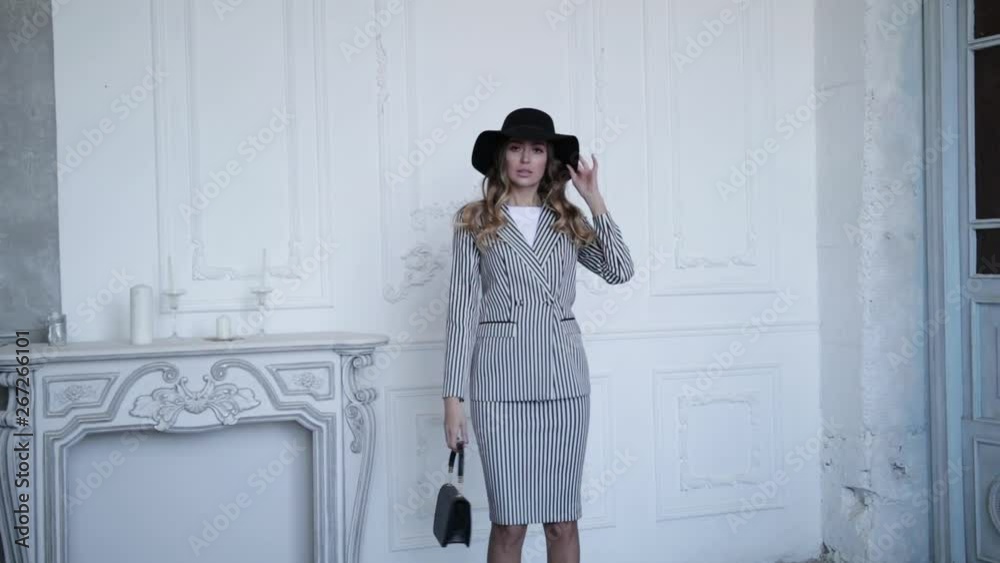 Gorgeous girl on the background of the fireplace, posing in a black hat with a bag and striped jacket and trousers . Slow motion Gorgeous girl on the background of the fireplace, posing in a black hat with a bag and striped jacket and trousers . Slow motion