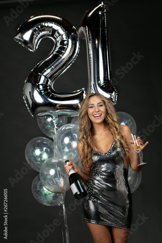 Beautiful young woman in party mini dress celebrating 21st birthday with champagne and balloons  