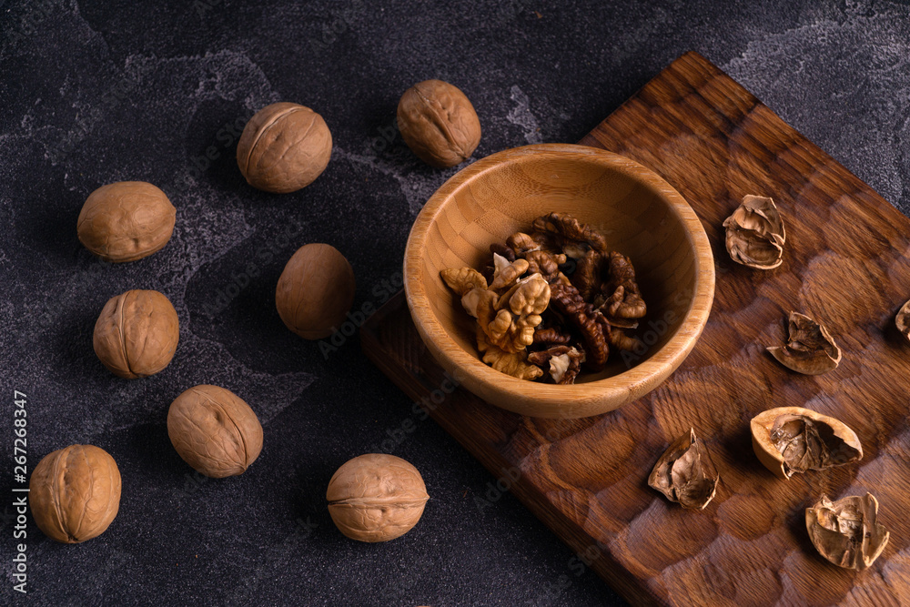 Walnut kernels in wooden bowl and whole walnuts on blue slate table. Healthy nuts and seeds composition. Walnut kernels in wooden bowl and whole walnuts on blue slate table. Healthy nuts and seeds composition.