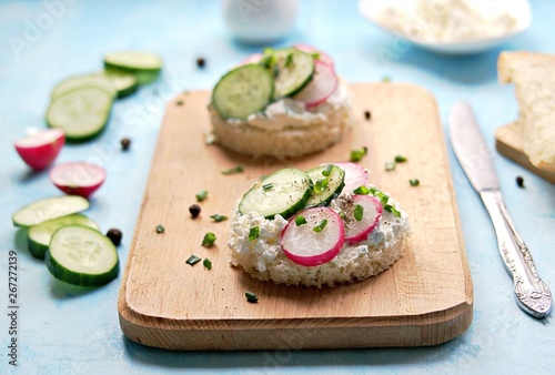 White bread sandwiches with salted cottage cheese, fresh radish and cucumber on a light blue background. Healthy food.