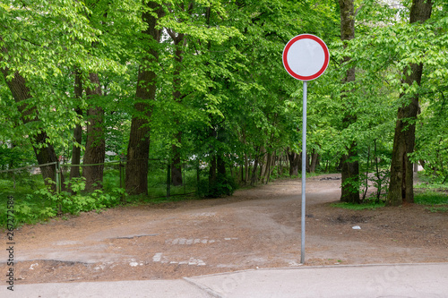 Blue and red road sign on a sunny day among green leaves