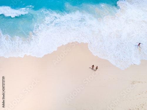 Top view from aerial. Bali drone shoot with ocean waves and white sand. People walk on beach
