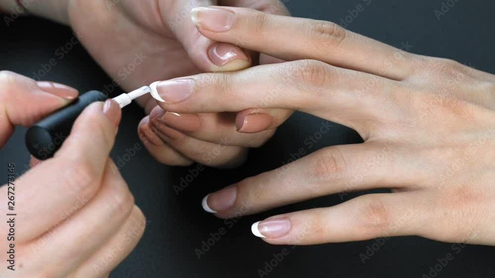 the manicurist paints the client's nails with nail polish on a black background Painting nails. Female hands with beautiful french manicure the manicurist paints the client's nails with nail polish on a black background Painting nails. Female hands with beautiful french manicure