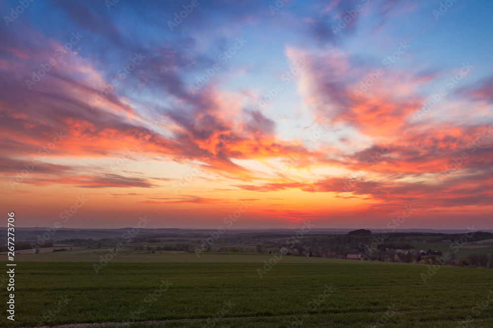 Obraz premium red sunset clouds over fresh green field with grass