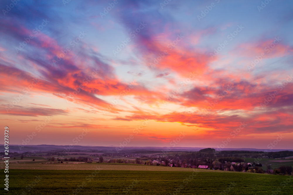 red sunset clouds over fresh green field with grass