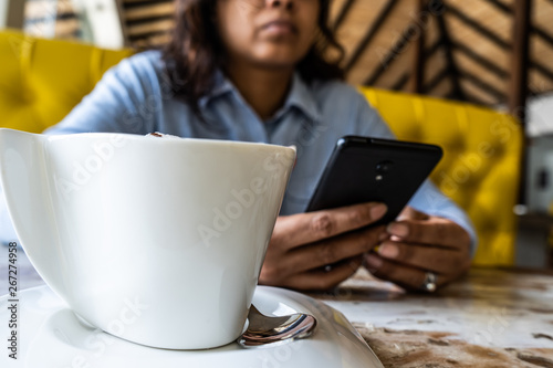 Woman using phone and drinking coffee in a cafe