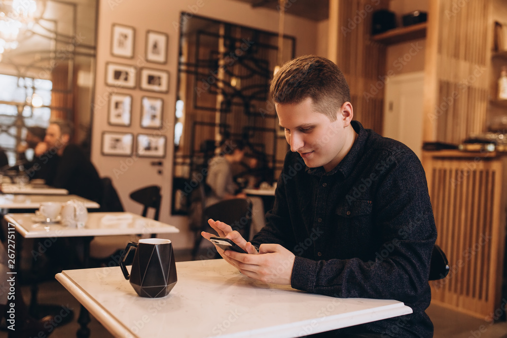 Handsome brutal business man student sitting in cafe drinking coffee in the morning, chating in social network by smartphone. Breakfast,  business, technology concept